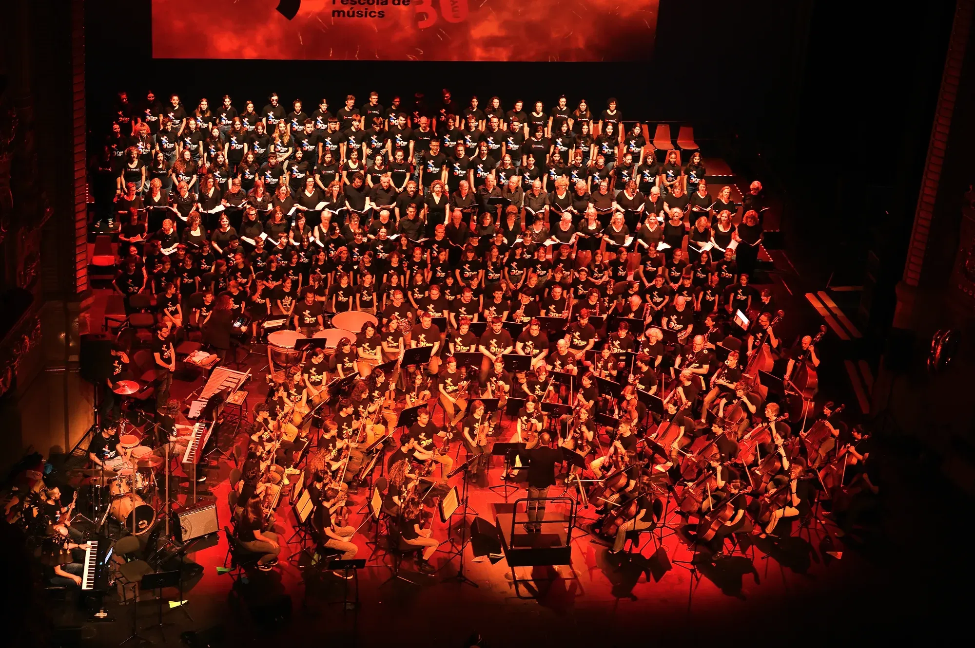Orquestra i cor nombrosos en un escenari il·luminat de vermell