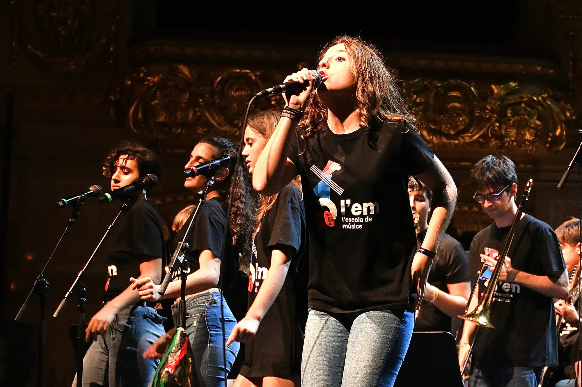 Alumnes d’un combo cantant en un escenari amb samarreta de l’escola
