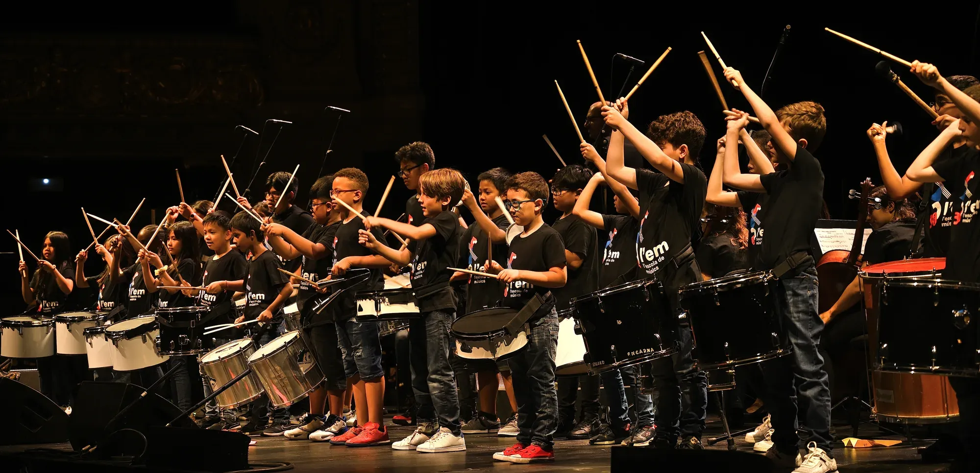 Alumnes tocant tambors amb les baquetes enlaire en un escenari
