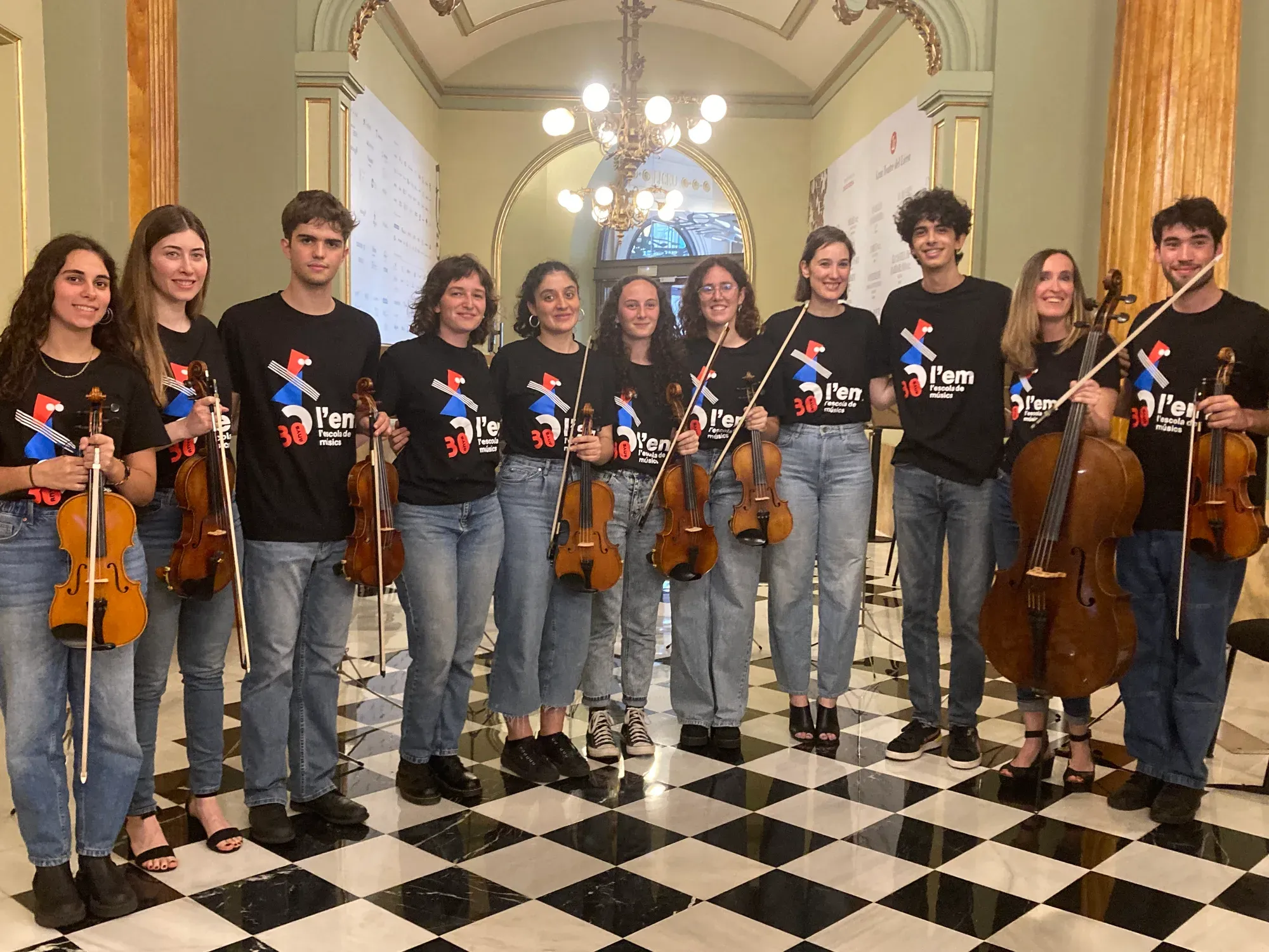 Alumnes de l’orquestra de cordes amb samarreta de l’escola i els seus instruments